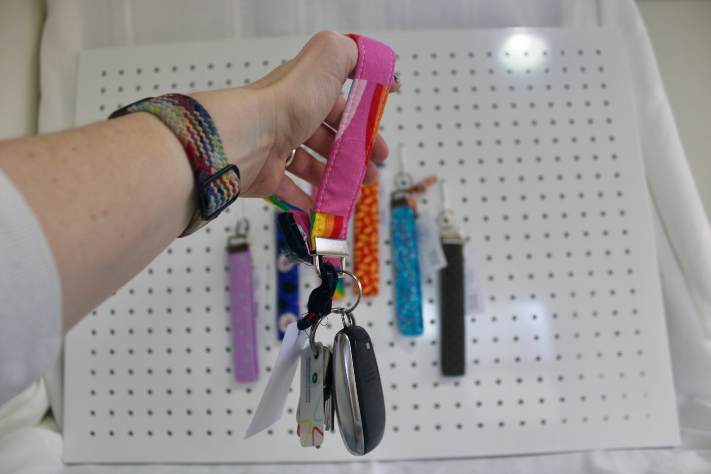 Hand holding a colorful keychain with keys against a pegboard background