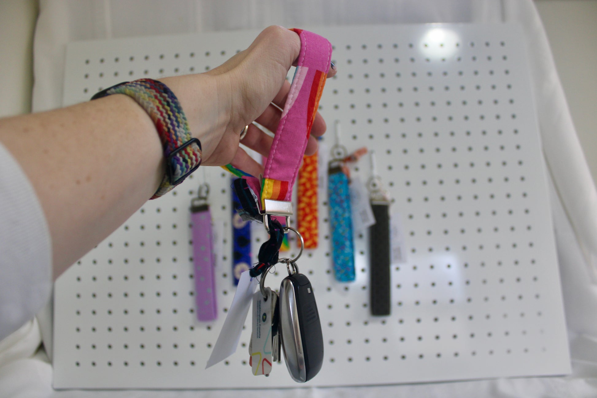 Hand holding a colorful keychain with keys against a pegboard background